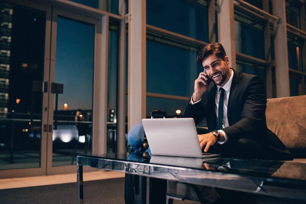 Smiling,Businessman,With,Laptop,Talking,On,Cellphone,At,The,Airport