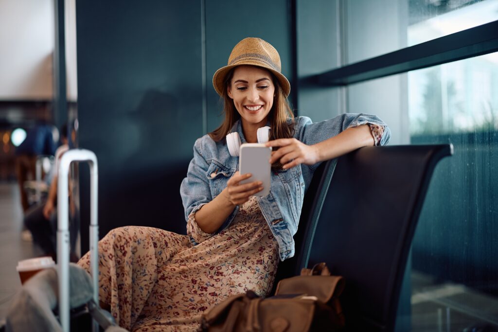 Happy,Woman,Using,Smart,Phone,While,Waiting,For,Her,Flight