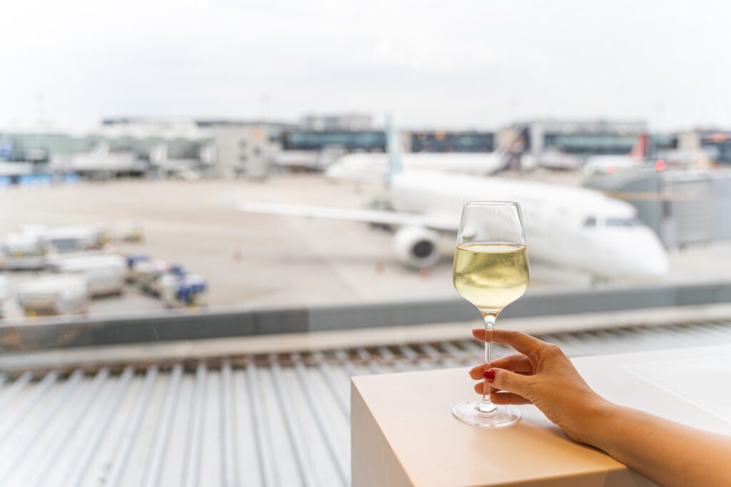 Female hand holding a glass of wine near window with a view to an aircraft